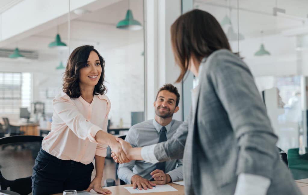 Smiling young businesswoman shaking hands with an office colleague