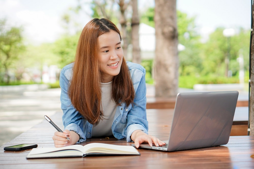 Young woman taking notes while smiling at laptop