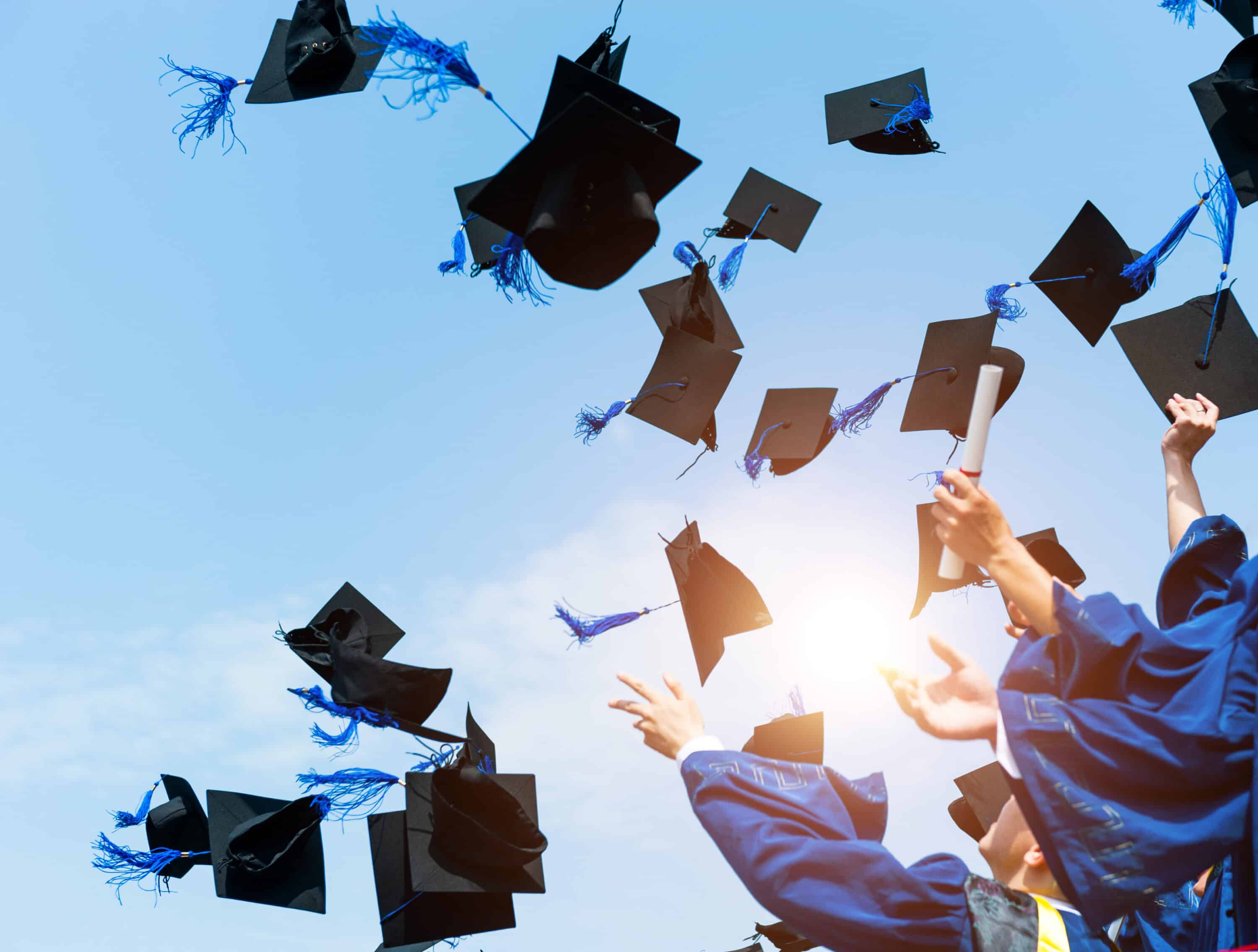 lots of graduation caps tossed above student heads in the sun